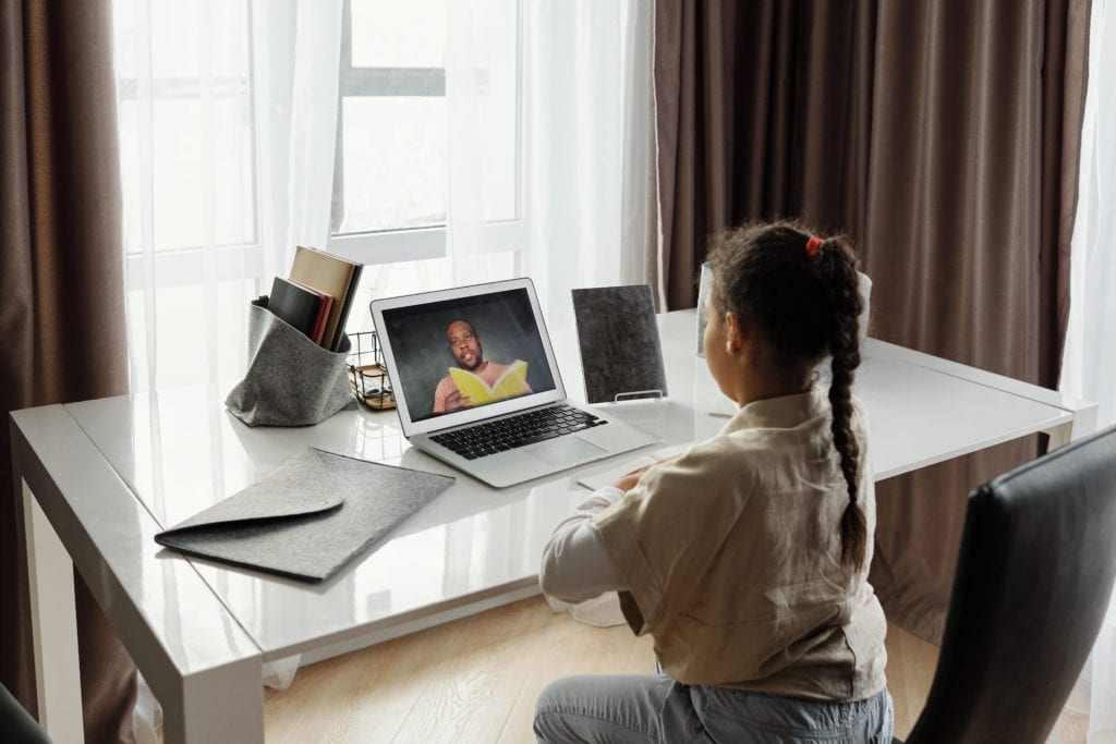 young girl sitting at desk doing telehealth therapy on laptop